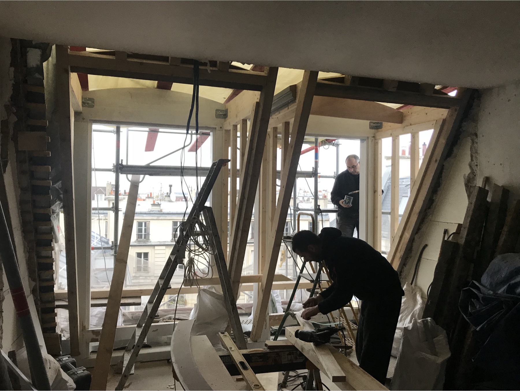 Charpentier au travail dans une lucarne en construction, toits de Paris au fond.